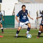 Jogadoras de futebol disputam uma partida ao ar livre.