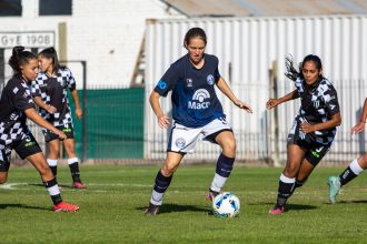 Jogadoras de futebol disputam uma partida ao ar livre.