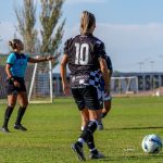 Jogadoras disputam uma partida de futebol feminino ao ar livre, sob luz do dia.