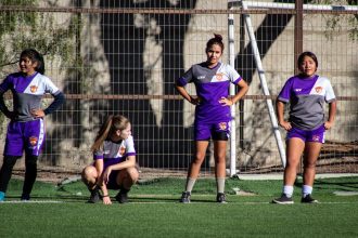 Grupo de jogadoras de futebol aquece em campo antes de uma partida.