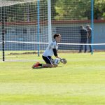 Goleira ajoelhada segura uma bola durante um treinamento de futebol ao ar livre.