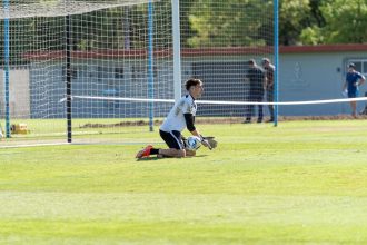 Goleira ajoelhada segura uma bola durante um treinamento de futebol ao ar livre.