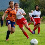 Jogadoras de futebol feminino disputam a bola durante uma partida em campo aberto.