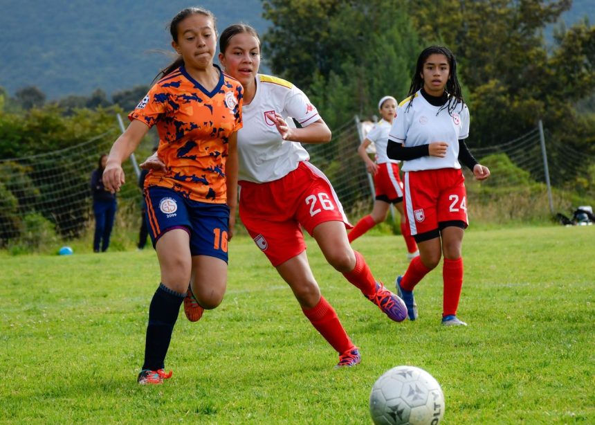 Jogadoras de futebol feminino disputam a bola durante uma partida em campo aberto.