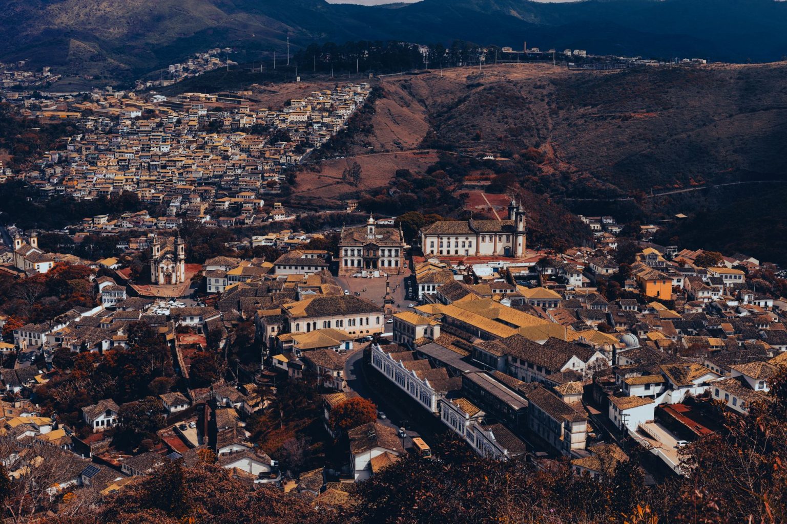 Vista aérea de Ouro Preto, com arquitetura histórica, áreas verdes e relevo montanhoso ao redor da cidade.