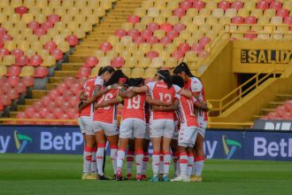 Jogadoras de futebol feminino reunidas em círculo no campo antes de uma partida.