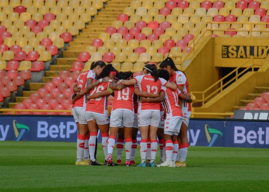Jogadoras de futebol feminino reunidas em círculo no campo antes de uma partida.