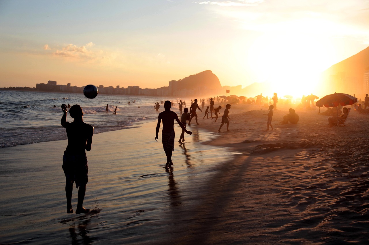Pessoas jogam futebol na areia à beira-mar, em uma praia do Rio de Janeiro.